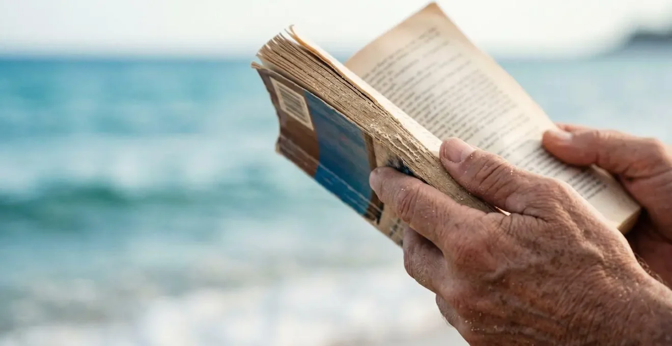 Gros plan sur des mains tenant un livre ouvert avec l'océan flou en arrière-plan